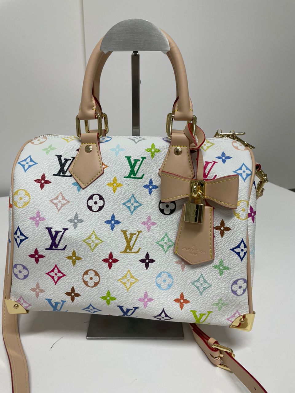 A Louis Vuitton monogram handbag in white coated canvas with multicolor printed monogram motifs, beige leather handles and trim, and gold-tone hardware, displayed on a stand against a plain light background.